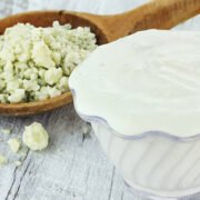 Bowl of freshly made blue cheese salad dressing with chunks of blue cheese in wooden spoon on a light rustic background.