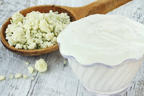 Bowl of freshly made blue cheese salad dressing with chunks of blue cheese in wooden spoon on a light rustic background.